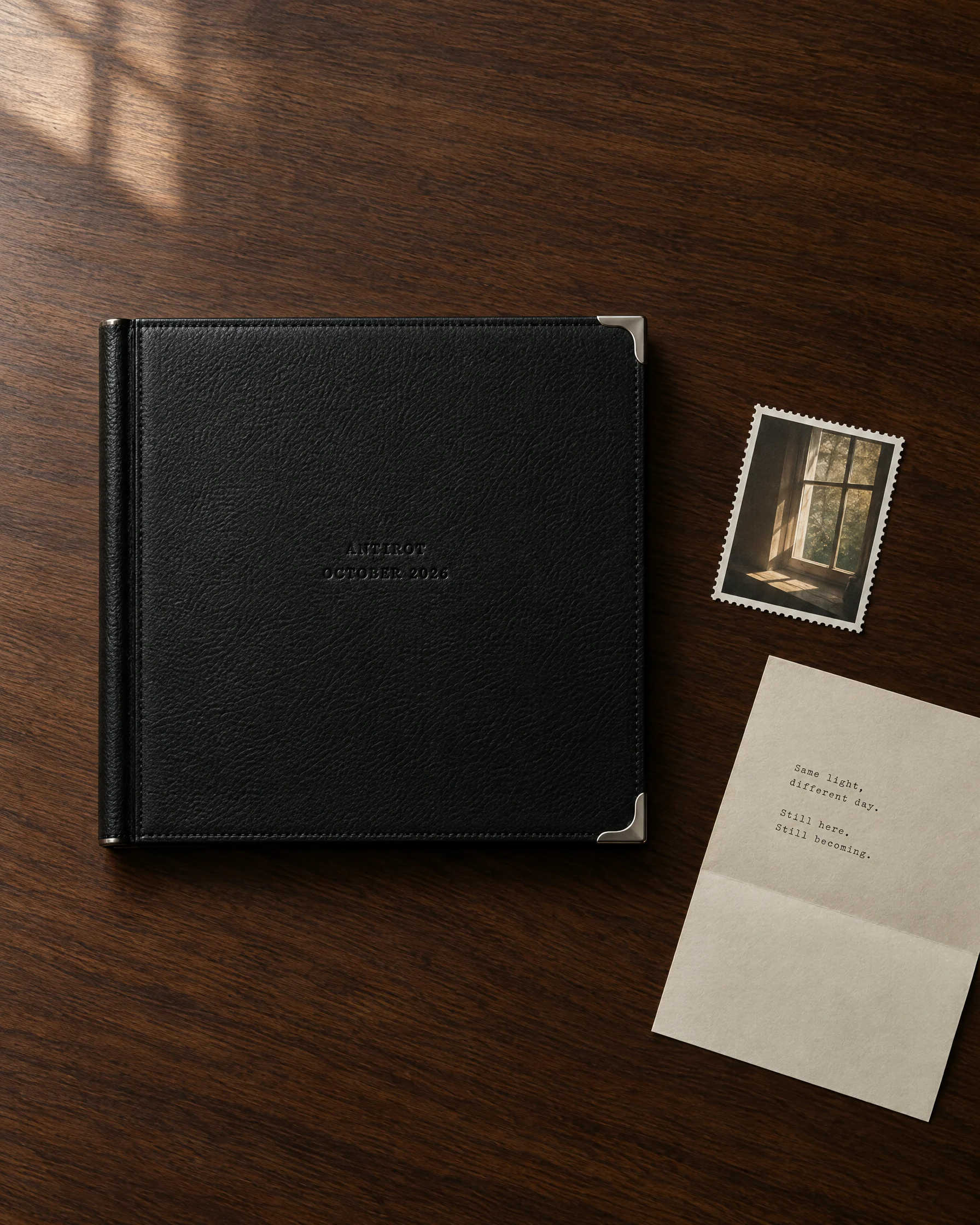 A black leather album with steel corners on a walnut desk.